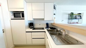 Una cocina compacta con armarios blancos, un microondas, una cafetera y un lavamanos.