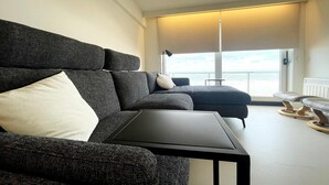 Un salón moderno con un sofá gris oscuro, una mesita negra y vistas al mar a través de amplios ventanales.
