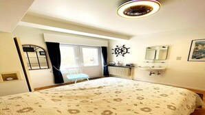 Een slaapkamer met een groot bed, een raam met gordijnen, een decoratie van een schipsschroef en een wastafel, plus een ingelijst schilderij aan de muur.