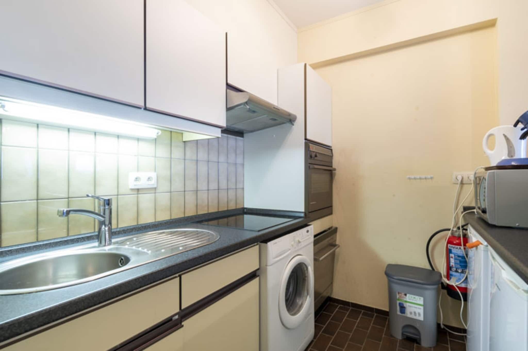 Une cuisine de taille réduite, équipée d’un évier, d’un lave-linge et d’une petite poubelle.
