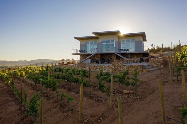 Un edificio moderno de dos pisos con fachada de piedra, ventanas grandes y un balcón con mobiliario exterior.