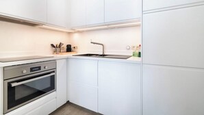Una cocina moderna con armarios blancos, horno de acero inoxidable, un lavamanos y una encimera con cafetera y utensilios.
