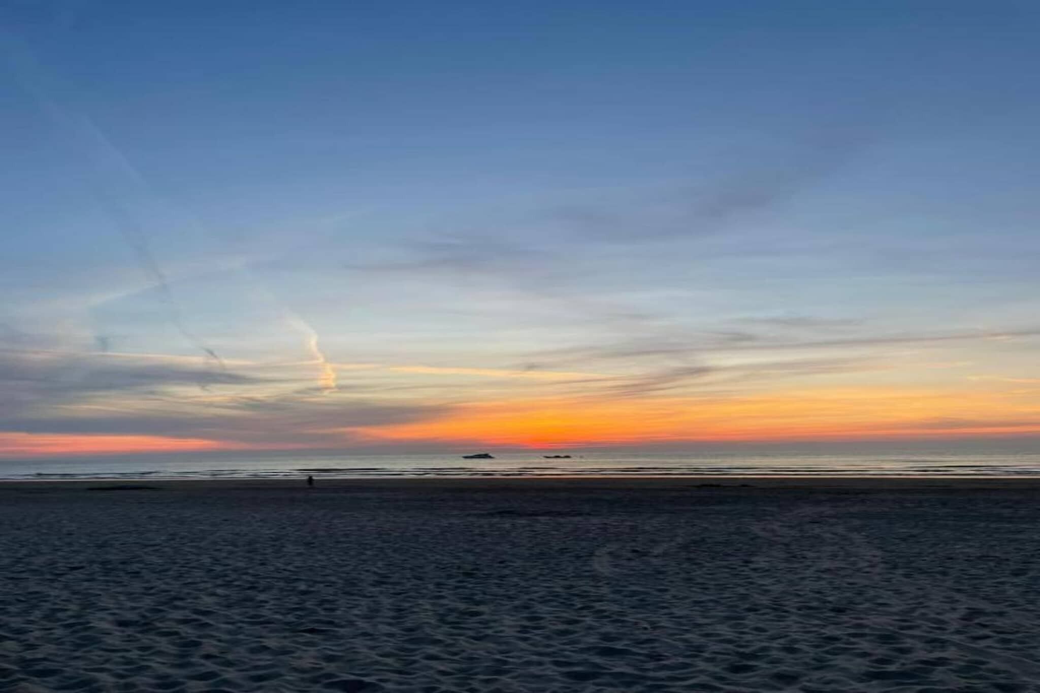 A beach with a sunset, clear sky, and calm sea.