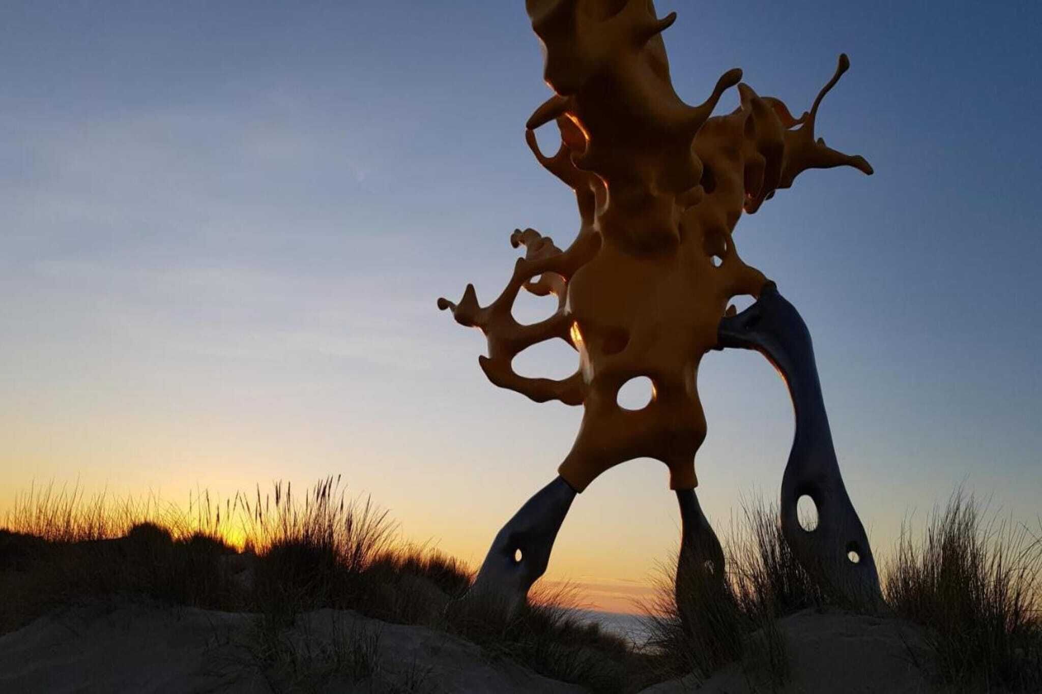A sculpture with a complex, abstract form, set against a sunset sky.