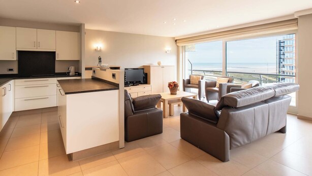 Een moderne woonkamer met een bank, een televisie en een balkon met uitzicht op zee.