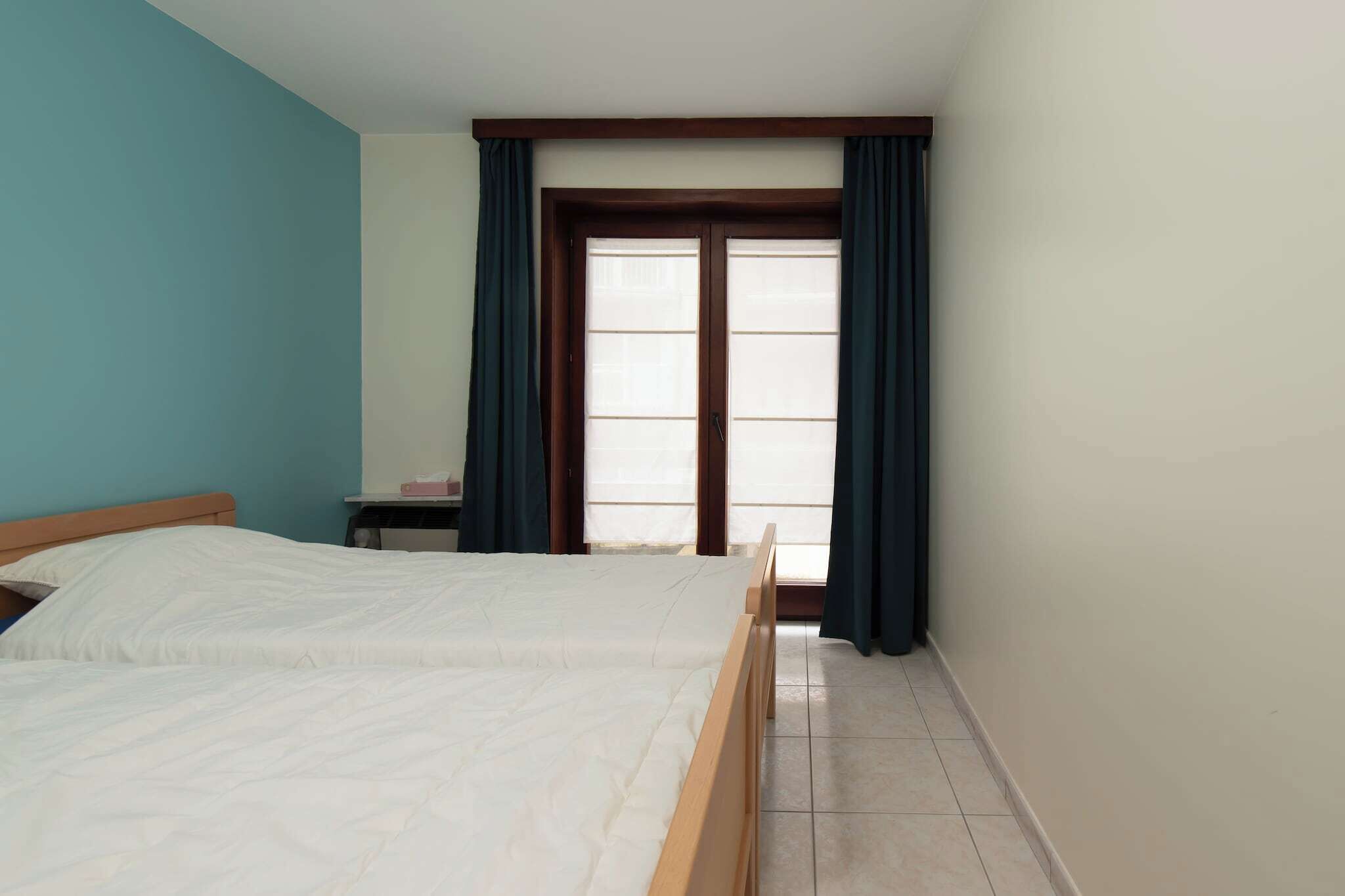 A bedroom with a bed, a nightstand, a window with curtains, and a view of the outside.