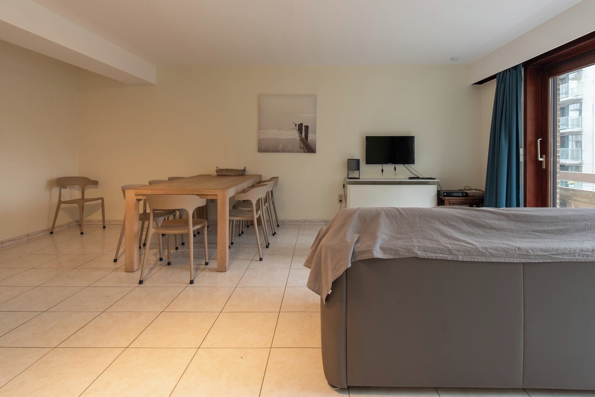 A hotel room with a bed, a desk with chairs, a television, and a window with curtains.
