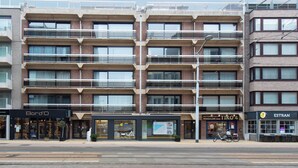 En bygning med flere etager og moderne arkitektur, med altaner, store vinduer og butikslokaler, herunder Bord'O, Tiko 4 og Estran.