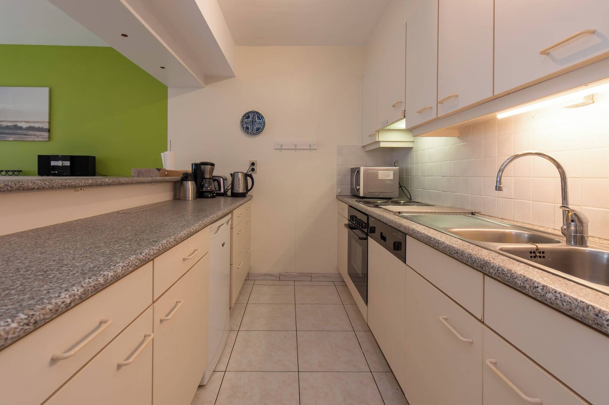 A compact kitchen with white cabinets, a granite countertop, a sink, a microwave, and a coffee maker.