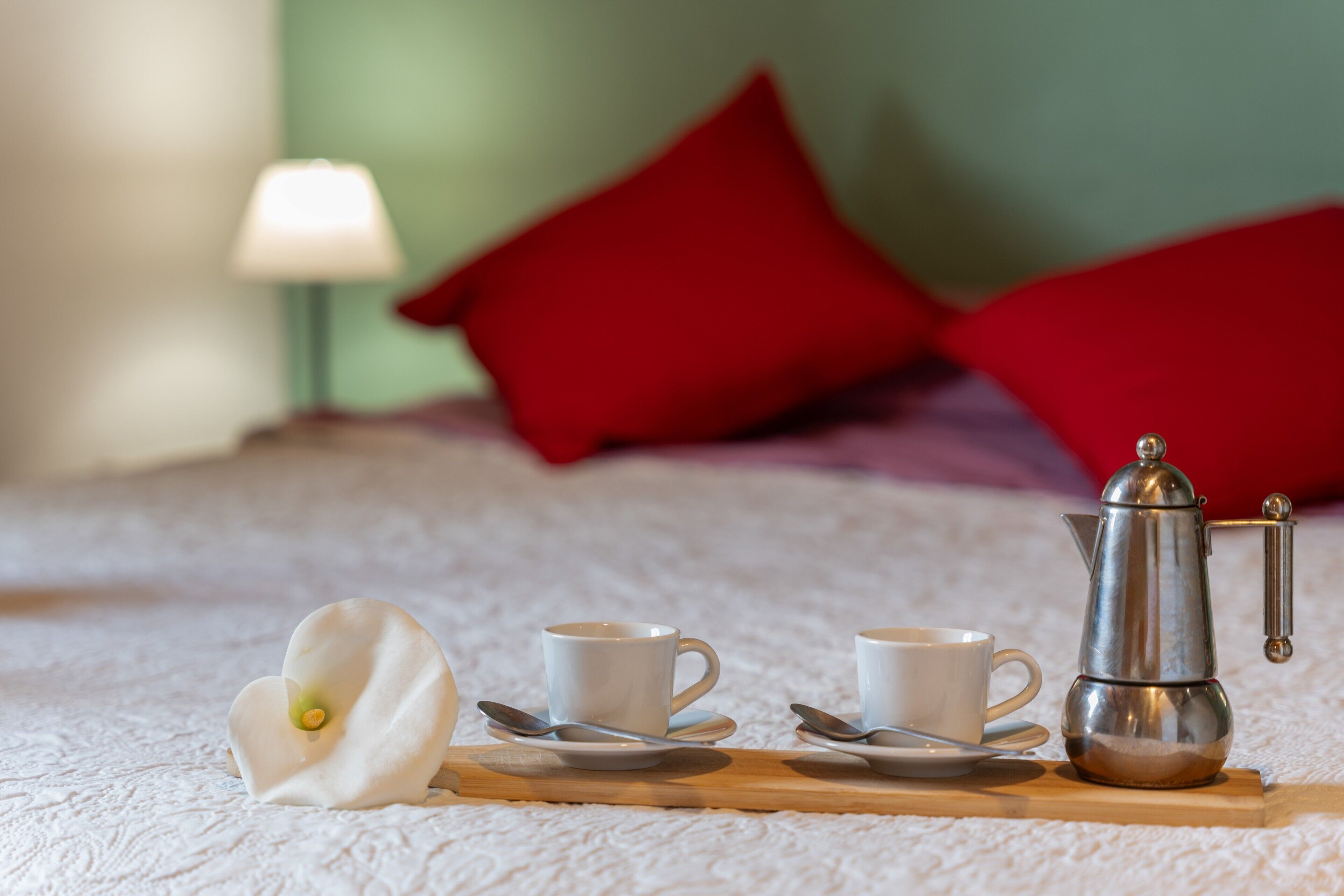 A neatly arranged breakfast setup on a bed with a coffee pot, cups, and a flower.