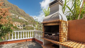 Een terras met een stenen vloer, een witte balustrade en een bakoven van baksteen.