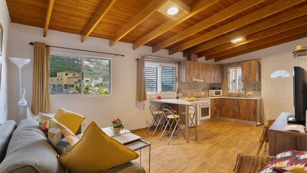 Een gezellige woonkamer met een bank, eettafel en stoelen, een keuken met houten kastjes en een koelkast, en een balkon met uitzicht op gebouwen.
