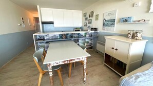 A compact kitchen with white cabinets, a dining table with chairs, and a small refrigerator. - Apartment by the Sea with Stunning Views (MIDDELKERKE)