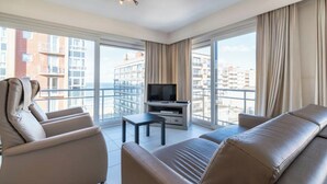 Une chambre d’hôtel moderne dotée d’une grande fenêtre, d’un téléviseur à écran plat, d’un canapé et d’une petite table.