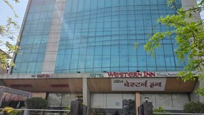 A hotel with a modern glass facade, a prominent sign for "WESTERN INN Family Hotel," and a set of stairs leading to the entrance. - HOTEL WESTERN INN (Vasai)