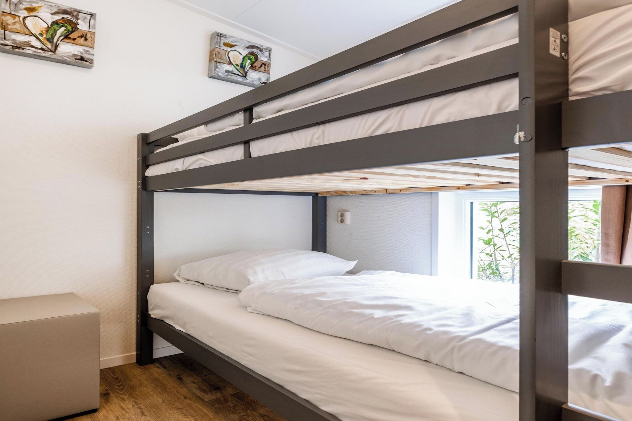 A bunk bed with white bedding, a small bedside table, and artwork on the wall.