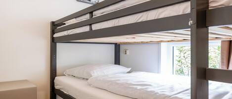 A bunk bed with white bedding, a small bedside table, and artwork on the wall.