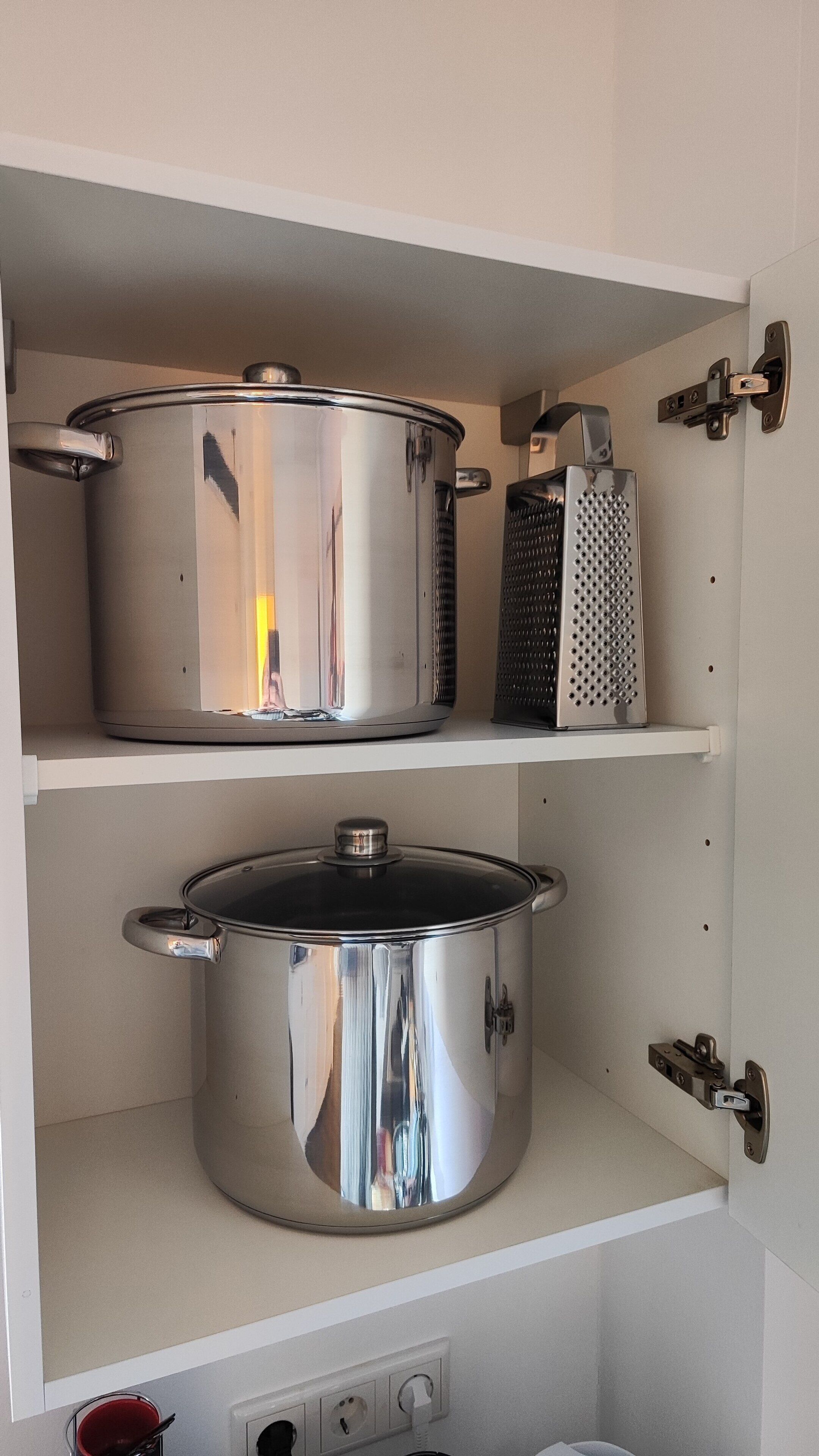 Un meuble de cuisine contenant deux casseroles en acier inoxydable et une râpe.