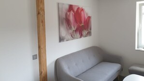 Una habitación con un sofá gris, una viga de madera y un cuadro con flores rosas colgado en la pared.