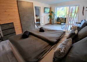 A room with a bed, a TV, a plant, and a view of the outdoors. - Apartment Flora – Idyllic Retreat with Private Terrace in Wahlwies (Stockach)