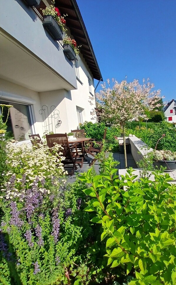 A building with a balcony, outdoor seating, and a garden with various plants.
