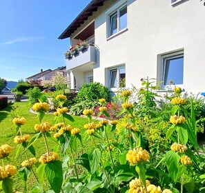 A residential building with a garden in front, featuring yellow flowers and a clear sky.
