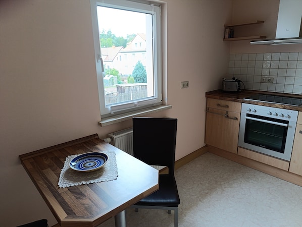 A small kitchen with a window, a table with a plate, a chair, a stove, and a toaster.