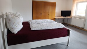 Un dormitorio con cama, un armario, un escritorio con computadora y una ventana con cortinas.