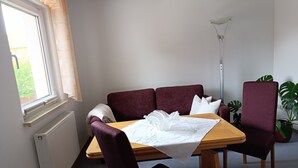 Un comedor con mesa, sillas, un radiador, una ventana con cortinas y una lámpara de pie.