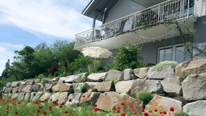 A modern building with a balcony, a stone wall, and a field of red poppies.