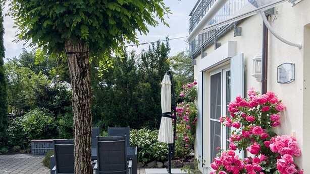 Ein Patio mit Gartenmöbeln, einem Baum und blühenden Pflanzen.