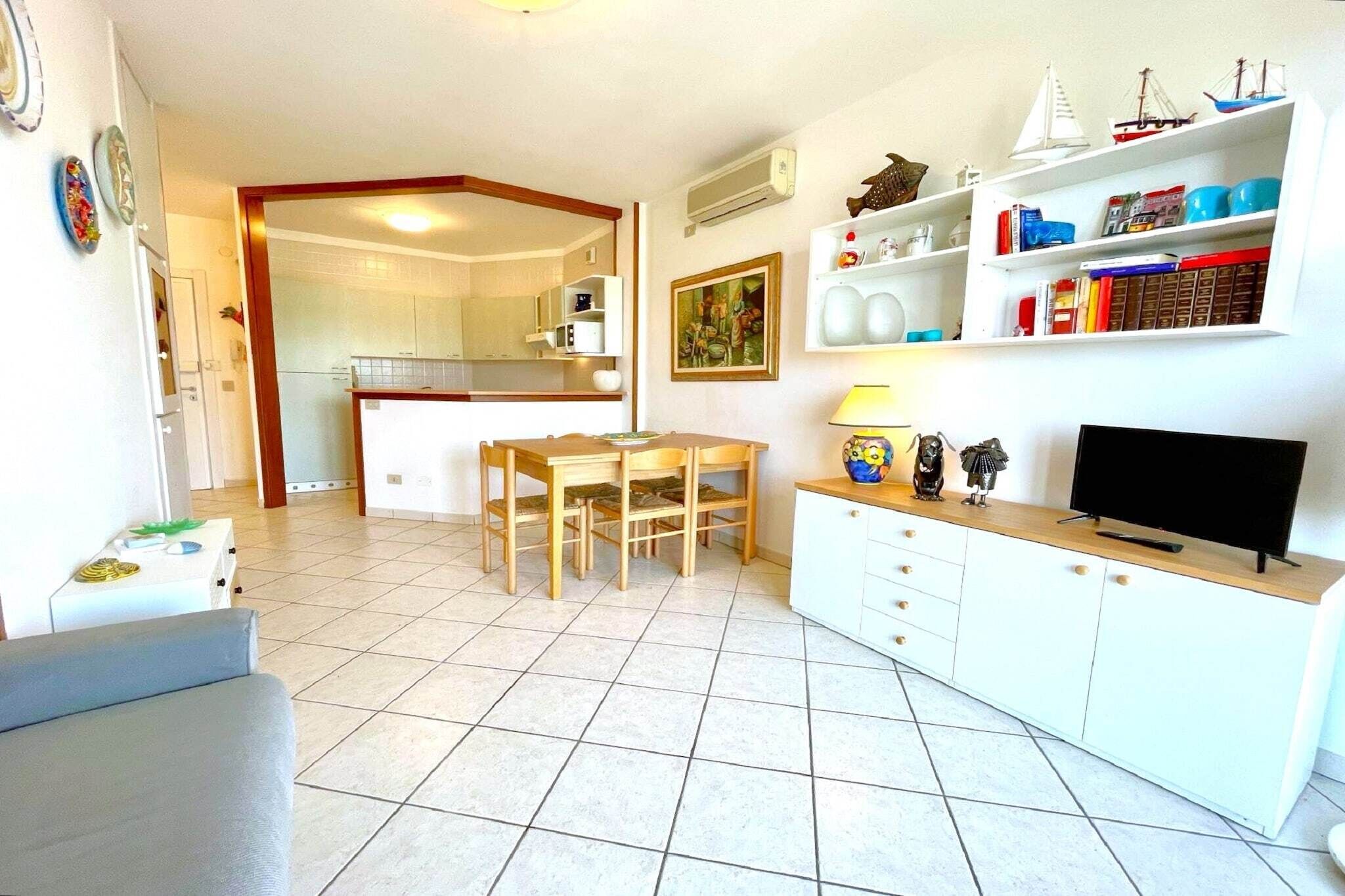 Een ruimtelijk ingerichte leefruimte met een eethoek, een televisie en een kitchenette.