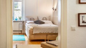 Un dormitorio con cama, ventana, radiador y una mesita.