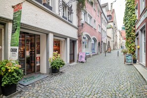 Una calle adoquinada con tiendas, un estandarte verde y plantas en macetas.
