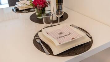 A table set with a placemat, a folded napkin with a message, a fork, a knife, and two wine glasses.