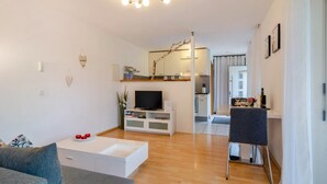 Un salon moderne avec un canapé blanc, une table basse, un téléviseur à écran plat et un coin repas comprenant une table et des chaises.