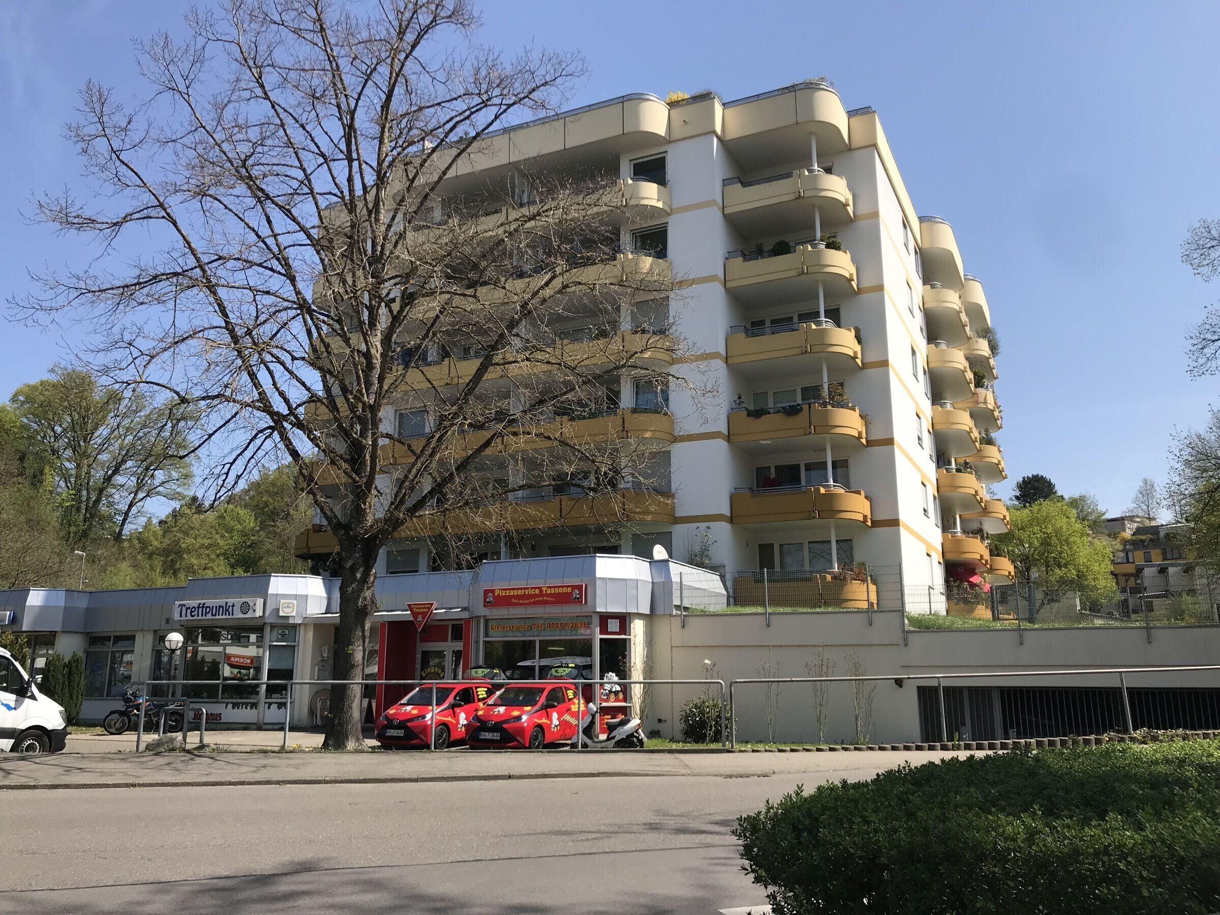 Ein mehrstöckiges Gebäude mit Balkonen, einem Pizza-Service-Schild und geparkten Autos.