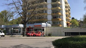 A multi-story building with balconies, a pizza service sign, and parked cars. - 'Saschas' Holiday Apartment with Lake View, Balcony, and Wi-Fi (Überlingen)