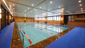 Une grande piscine intérieure dotée de plusieurs couloirs, entourée d’un sol bleu et de murs en bois.