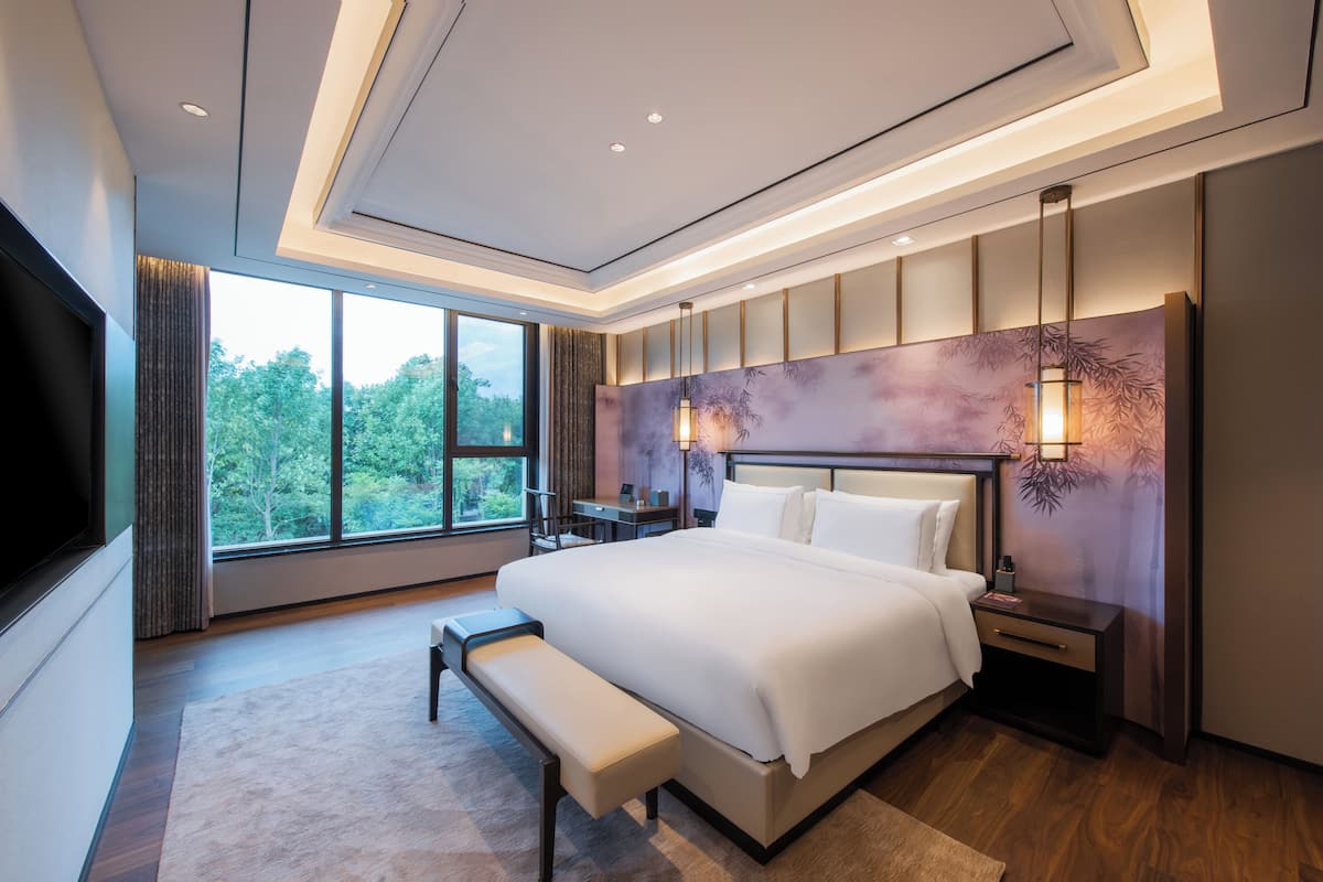Ein modernes Hotelzimmer mit einem großen Bett, einer Bank, einem Schreibtisch und einem Fernseher.