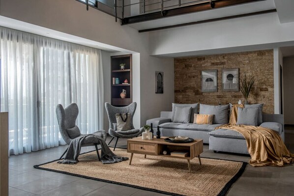 A modern living room with a grey sofa, two armchairs, a wooden coffee table, and a bookshelf.