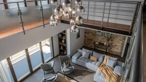 A modern loft apartment with a mezzanine, large windows, a hanging spherical light fixture, and a stone accent wall. - Villa Ete: Prime 4BR Retreat with Private Pool (Stalida)