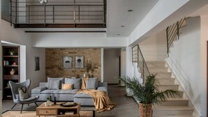 A spacious living room with a grey sofa, a wooden coffee table, and a large woven rug. A staircase with a metal railing leads to an upper level. - Villa Ete: Prime 4BR Retreat with Private Pool (Stalida)