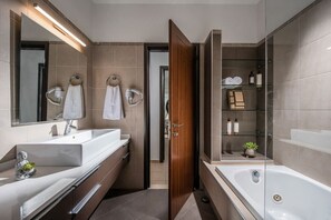 A modern bathroom with a large mirror, two sinks, a bathtub, and a glass shower enclosure.