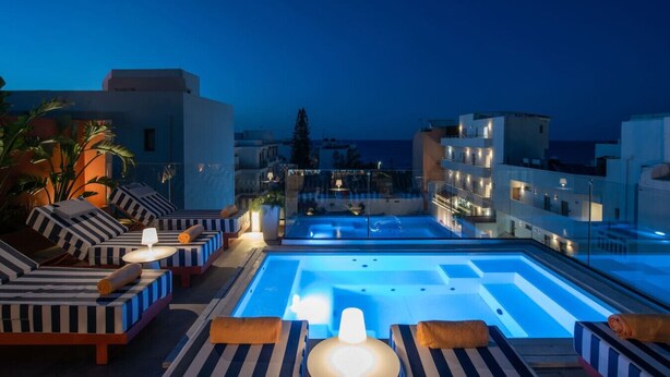 A rooftop pool area with lounge seating and a view of the cityscape at dusk.