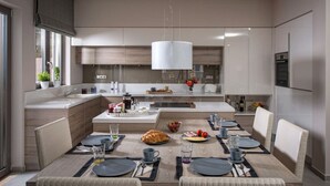 A modern kitchen with a central island, dining area with a table set for four, and a large window providing natural light. - Villa Belamar – Luxury Sea-View Stay, Hersonissos (Hersonissos)