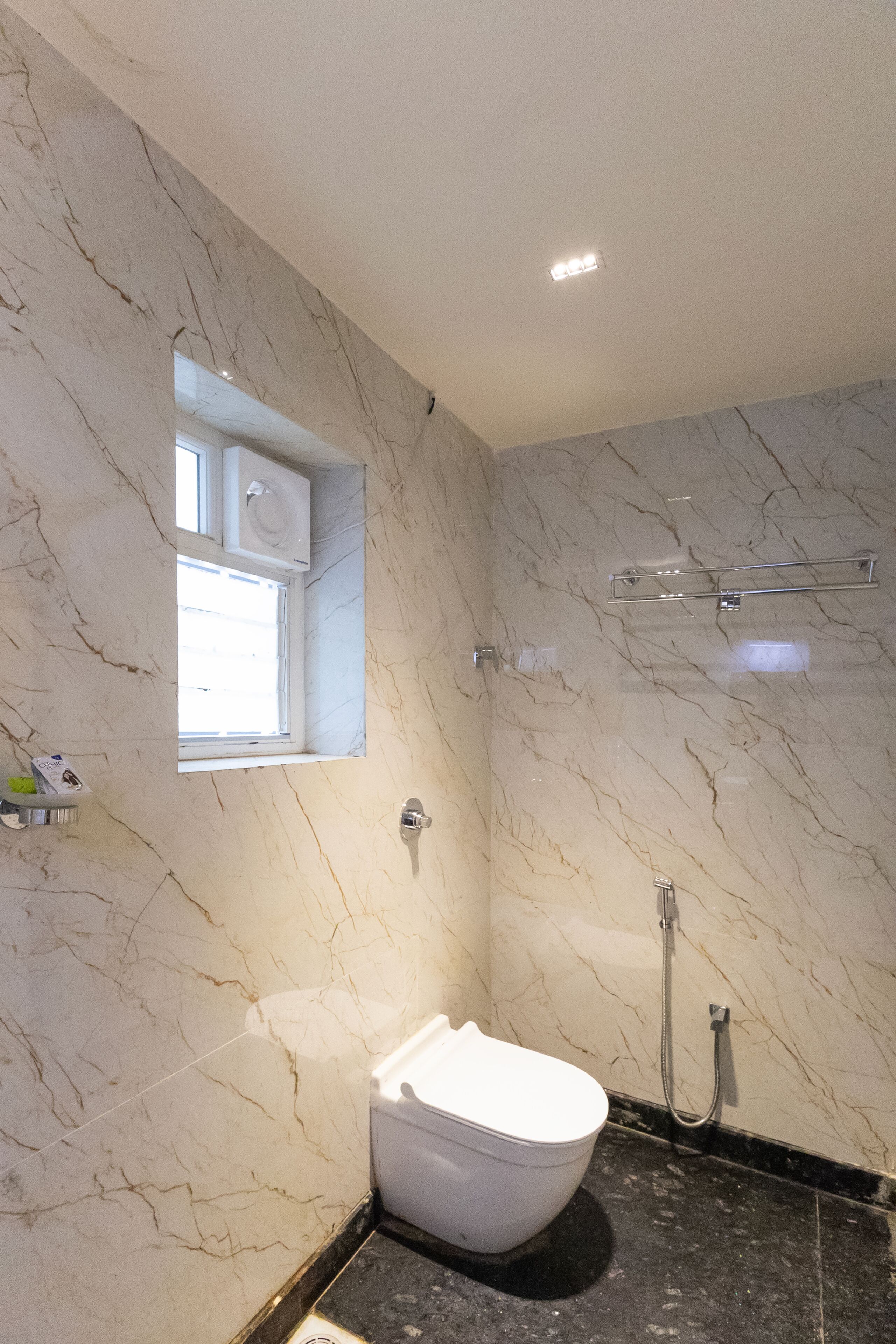 A bathroom with a marble wall, a toilet, a shower, and a small window.
