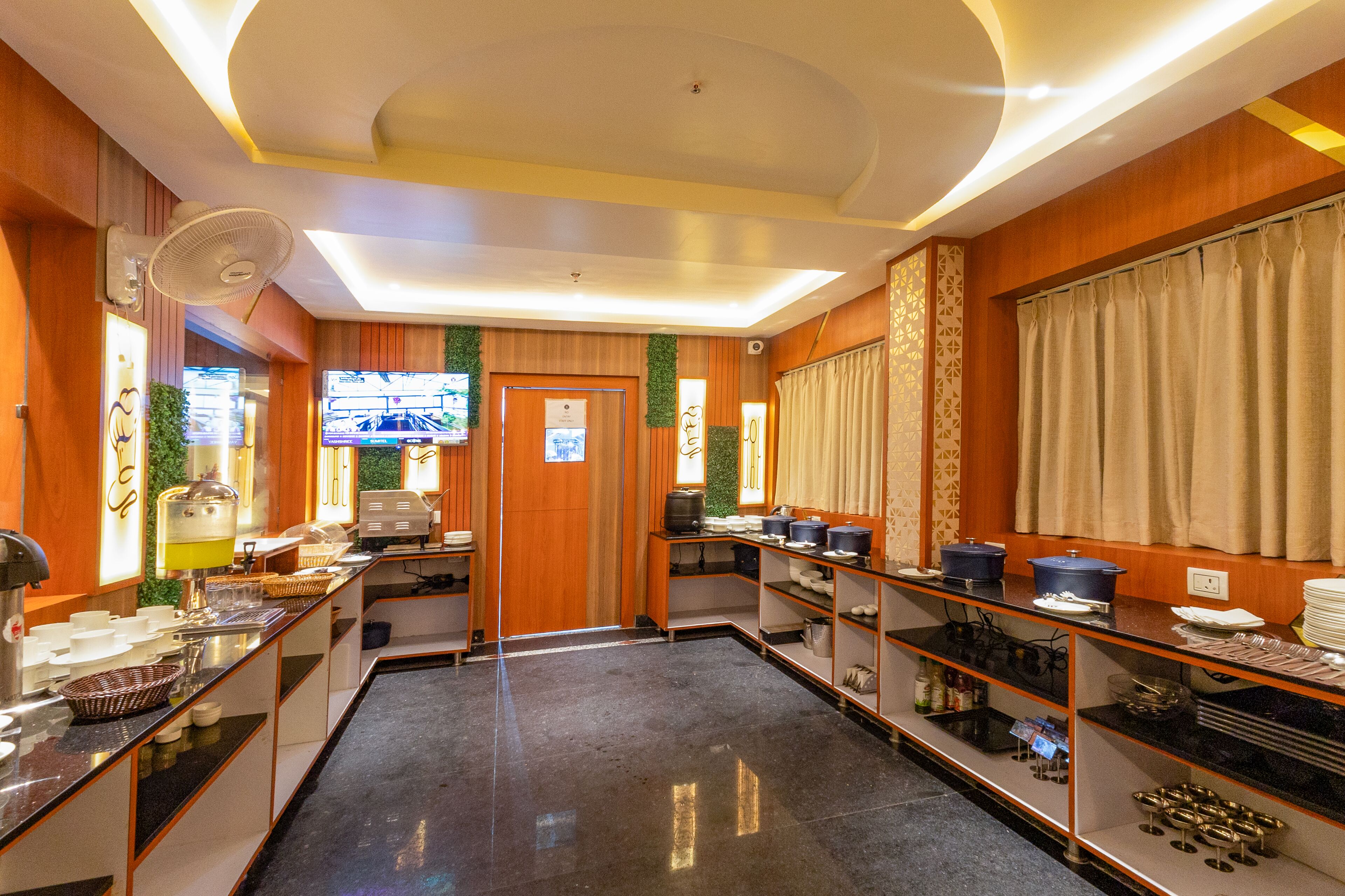 A hotel kitchen with buffet setup, wooden paneling, and a television screen.