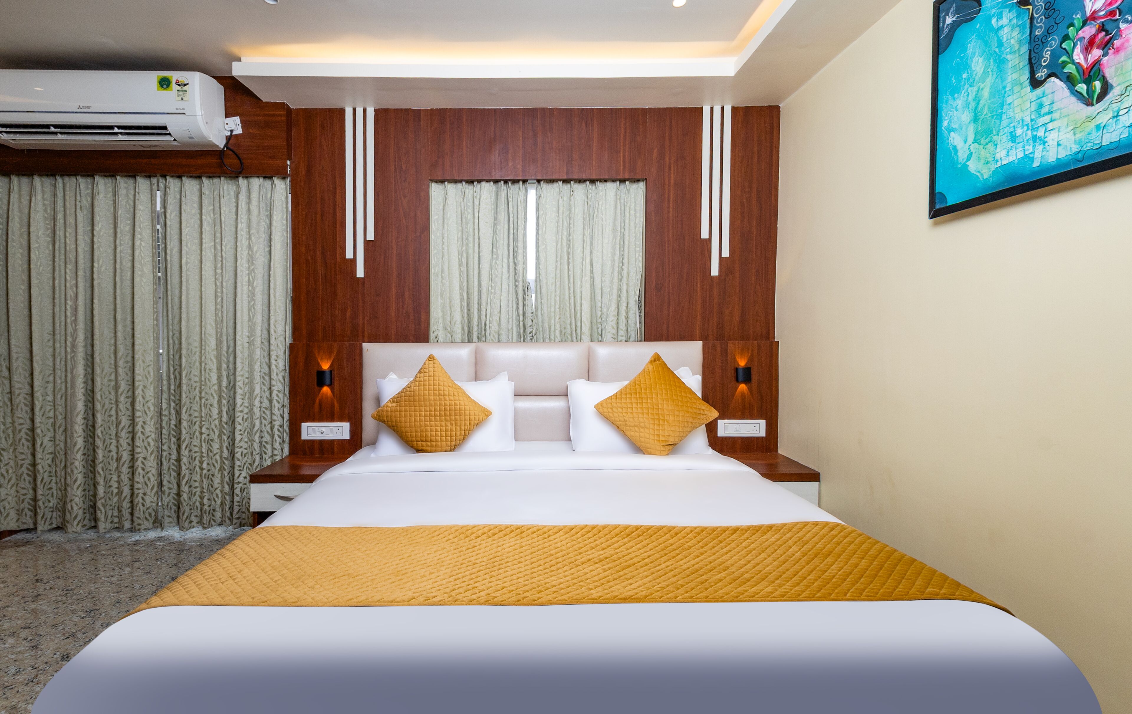 Habitación de hotel con una cama grande, cabecera de madera, dos mesitas de noche con lámparas y un cuadro en la pared.