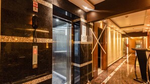A modern hotel lobby with marble flooring, an elevator, and a reception desk. - Yashshree Bangla Queen (Kanthi)